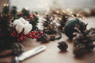 fir branches, wreath, red berries, pine cones, thread, scissors, cinnamon, cotton, lights on rustic 