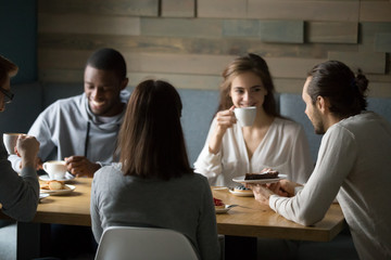 Wall Mural - Happy diverse friends having fun in coffeeshop enjoying coffee and desserts, smiling multiethnic young people laughing at joke, spending great time together in cafe, millennial colleagues meeting out