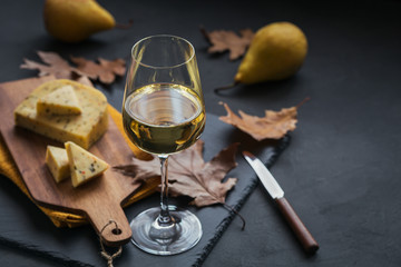 Wall Mural - A glass of white wine served with cheese in a cutting board on dark background