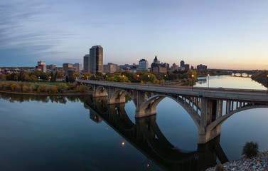 Aerial panoramic view of a bridge going over Saskatchewan River during a vibrant sunrise in the Fall Season. Taken in Saskatoon, SK, Canada.