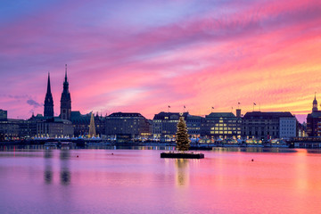 Sunset in Hamburg. Panoramic view of the decorated city center from Alster Lake, view to Hamburg Rathaus and a christmas tree installed in the center of the lake. Atmosphere before the New Year.