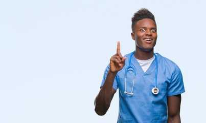 Poster - Young african american doctor man over isolated background wearing surgeon uniform pointing finger up with successful idea. Exited and happy. Number one.