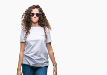 Sticker - Beautiful brunette curly hair young girl wearing sunglasses over isolated background with serious expression on face. Simple and natural looking at the camera.