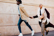 © BONNINSTUDIO/Stocksy - Cool multiethnic couple holding hands running on the street.