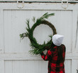 © Tana Teel Photography/Stocksy - young woman hangs festive holiday wreath on barn door