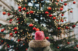 © Sanja Lydia/Stocksy - Girl with green parka and pink beanie standing in front of a christmas tree