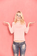one young smiling woman, questioning with her arms raised, posing and looking forward to camera, with her eyeglasses tilted, 20-29 years old, long blond hair. Shot in studio on pink background.