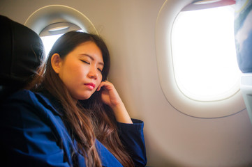  young happy and beautiful Asian Chinese woman traveling for business inside airplane cabin sleeping during long flight in air transportation concept