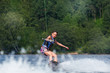 Young pretty slim brunette woman riding wakeboard on wave of motorboat in summer lake