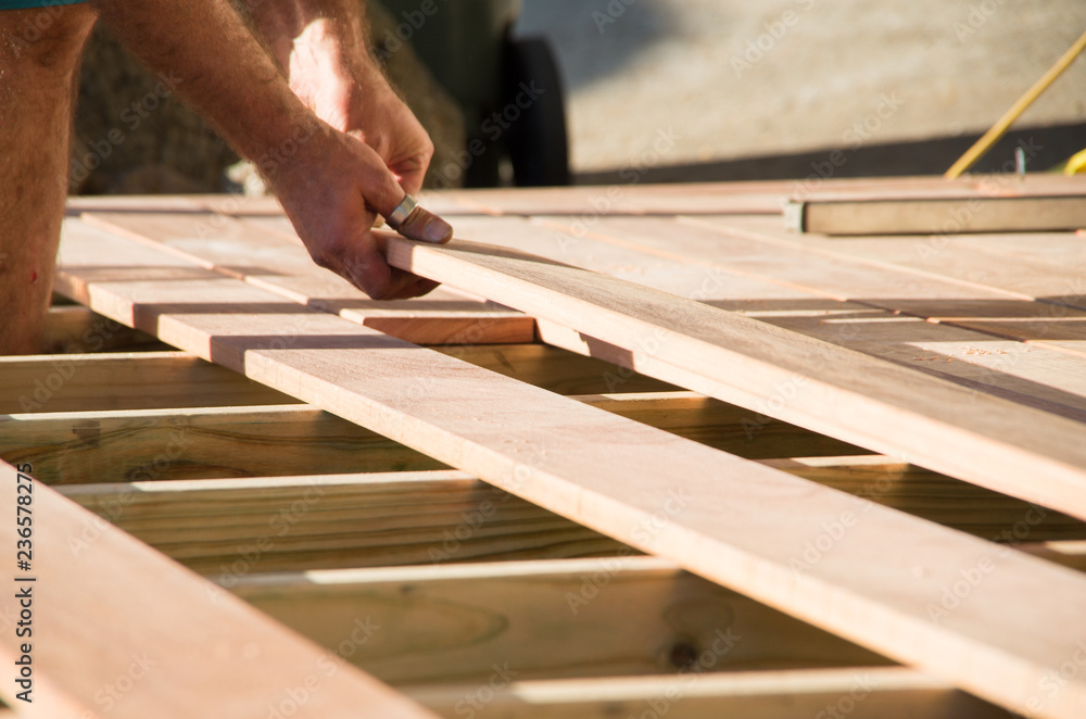Man placing a plank of wood in a deck home renovation - obrazy, fototapety, plakaty 