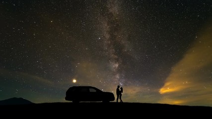 Wall Mural - The man and woman standing near a car on a meteor shower background. time lapse