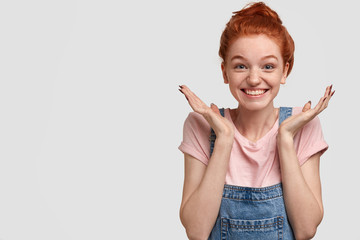 Glad freckled female spreads palms near face, smiles broadly, excited to notice best friend, dressed in casual clothes, isolated over white background with free space for your advertising content