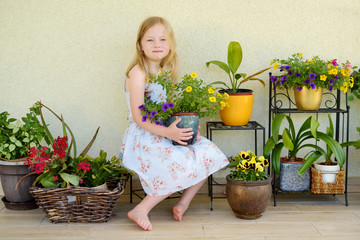 Wall Mural - Cute little girl sitting by flower pots on sunny summer evening.