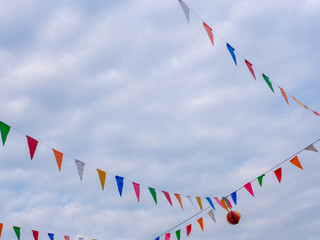 Row of colorful triangles flags on blue sky with clouds background in carnival fair