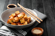 Fried tofu with sesame seeds and spices on black background.