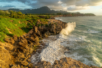 Wall Mural - Waves Breaking into Makawehi Bluff while warm sunrise light illuminates the clouds, Kauai, Hawaii