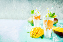 Tropical Sweet Dessert Drink. Mango Milkshake Or Smoothie Cocktail, With Mango Slices, Mint And Ice Cubes, Light Blue Background Copy Space