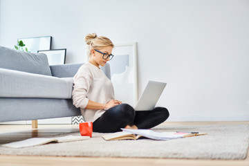 young woman sitting on floor at home working with laptop and documents