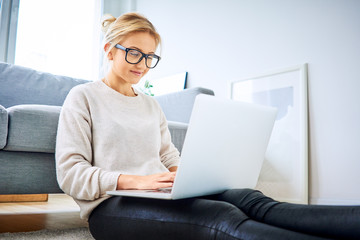 Beautiful woman sitting on floor at home and using laptop