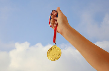 Wall Mural - woman hand raised, holding gold medal against sky. award and victory concept.