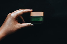 Female Hand Holding Container With Green Cream On Black Background
