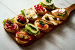 wooden board with colorful healthy mini sandwiches or tapas on a light wooden table