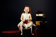 © Carlos David - Portrait of a smiling  toddler girl holding a shiny red gift, isolated on black studio background