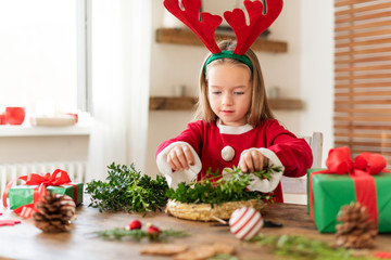 cute preschooler girl dressed in reindeer costume wearing reindeer antlers making christmas wreath i
