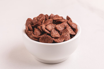 Crunchy chocolate corn flakes in bowl on light marble background