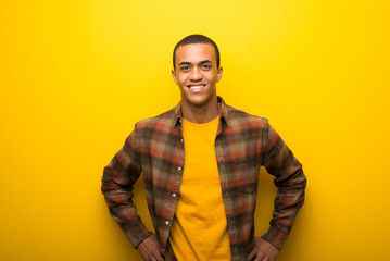 Wall Mural - Young african american man on vibrant yellow background posing with arms at hip and laughing looking to the front