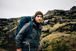 © BublikHaus - Smiling and happy portrait of young handsome traveller or hiker enjoying the outdoors activity. Wears winter jacket and beanie, together with backpack for tent and gear. Nomad lifestyle