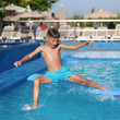 © Artem - Caucasian boy having fun making fantastic jump into swimming pool at resort. His arms and legs are wide open.