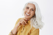 Close-up Shot Of Happy Delighted And Accomplished Charming European Elderly Female With White Hair In Yellow Trench Coat Touching Face Gently Laughing From Joy Feeling Pretty And Energized
