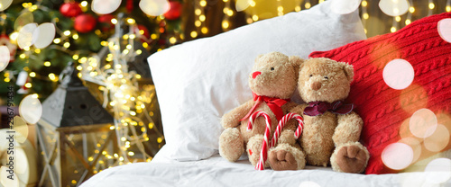 Cuadros en Lienzo Two teddy bears siting on the bed with red candys near christmas tree