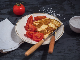 Breakfast of scrambled eggs and red pomomors, cut into slices, cutlery, salt shaker with coarse salt, linen napkin