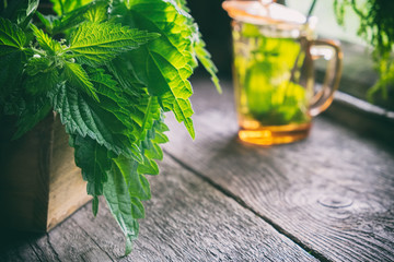 Wall Mural - bunch of a nettle plants in a wooden box and glass of healthy nettle tea not in focus on old wooden 