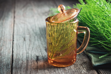 Wall Mural - Vintage glass cup of healthy tea  and bunch of horsetail herbs on old wooden table. Herbal medicine. Copy space for text.