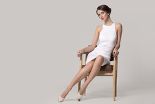 Fashionable Woman In A White Dress Is Sitting On A Chair. Bright Makeup