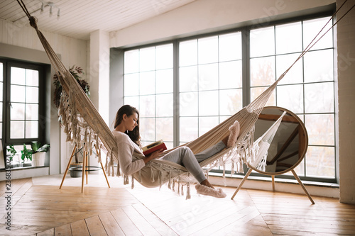 Photo  Dark-haired girl dressed in pants, sweater and warm slippers reads a book lying