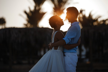 Beautiful smiling young bride and groom walking on the beach, kissing and having fun, wedding ceremony near the rocks and sea. Wedding ceremony on coast of Cyprus