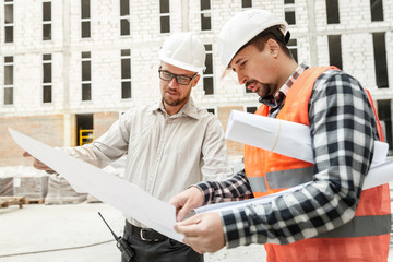 Male architect and developer with blueprints  discussing architect project at construction site.