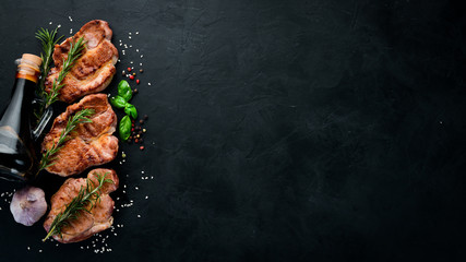 Meat steaks with rosemary. Grill, barbecue. On a black stone background. Top view. Free copy space.