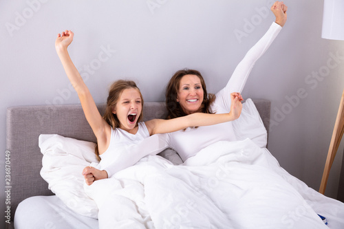 Fotografie, Obraz Mother And Daughter Stretching Their Arms On Bed
