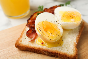 Toast with soft boiled egg and bacon on wooden board, closeup