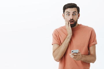 Oh no, wrong number. Portrait of man accidently sent message via smartphone wrong person touching face and open mouth troubled and concerned standing shocked, holding mobile phone in hand