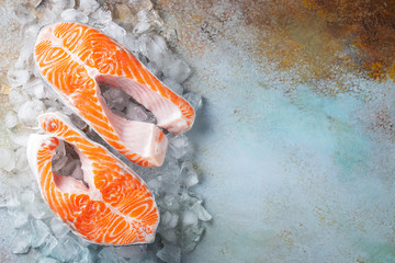 Two raw fresh salmon or trout steaks on ice, rich in omega-3 oil, with lime, thyme and olive oil on a blue rusty background. Healthy and diet food. Top view with copy space. Flat lay