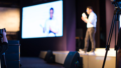 Fototapete - Presenter Presenting Presentation to Conference Audience. De-focused Blurred . Lecturer on Stage at Tech Forum. Speaker Giving Speech in Conference Hall Auditorium. Copy Space Screen Background.