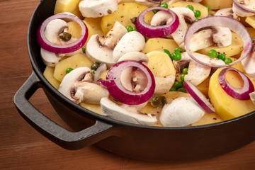 Wall Mural - A closeup photo of a pan with raw vegetables, potatoes, onions, green peas, and mushrooms, a vegan dinner