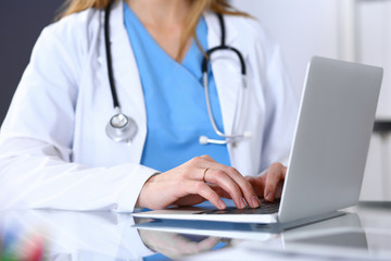 Doctor typing on laptop computer while sitting at the glass desk in hospital office. Physician at work. Medicine and healthcare concept