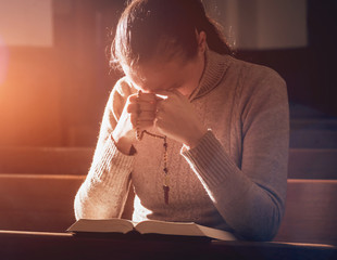 Wall Mural - Christian woman praying in church. Hands crossed and Holy Bible on wooden desk.